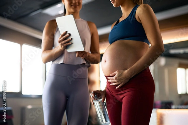 Fototapeta Close up of pregnant woman and her fitness instructor using touchpad at health club.