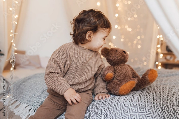 Fototapeta A small child, a toddler, is playing with a teddy bear. Trendy brown colors