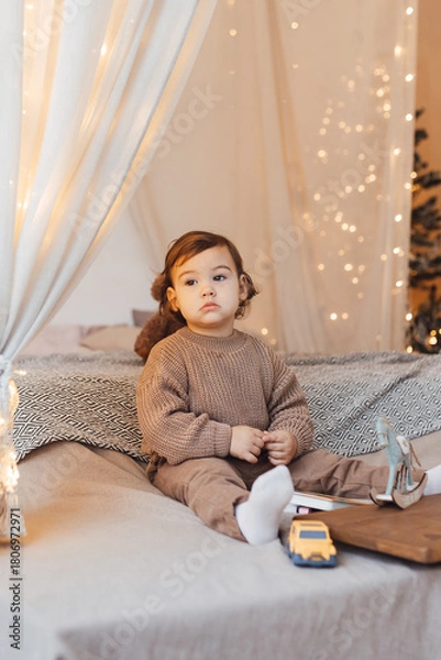 Fototapeta Little boy playing with a toy. Child is sad sitting on the bed. Brown colors.