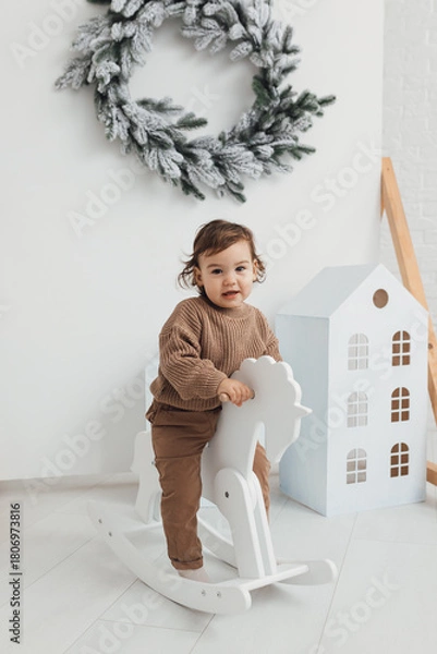Fototapeta Little boy playing with toy horse. Child swinging on a rocking horse on a white background