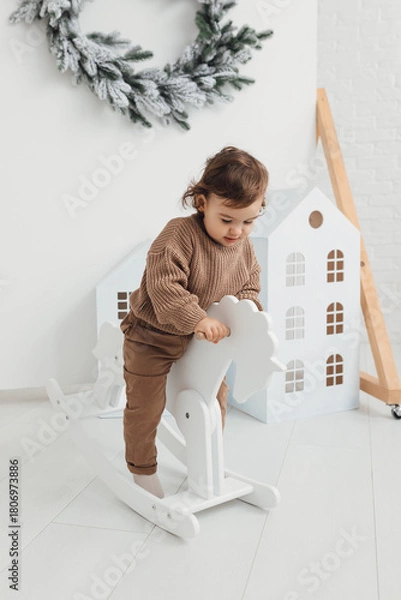 Fototapeta Little boy playing with toy horse. Child swinging on a rocking horse on a white background