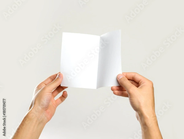 Fototapeta Male hands holding a white sheet of paper. Isolated on gray background. Closeup