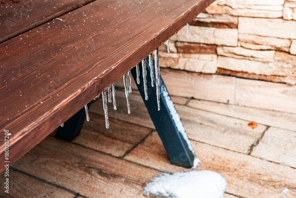 Fototapeta Icicles hanging from a wooden table on a stone patio. Snow is present on the ground, creating a winter scene