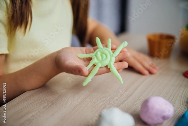 Fototapeta A little girl makes figurines out of colored airy plasticine, modeling dough. Hobbies for children's creativity, educational activities, development of fine motor skills of hands.