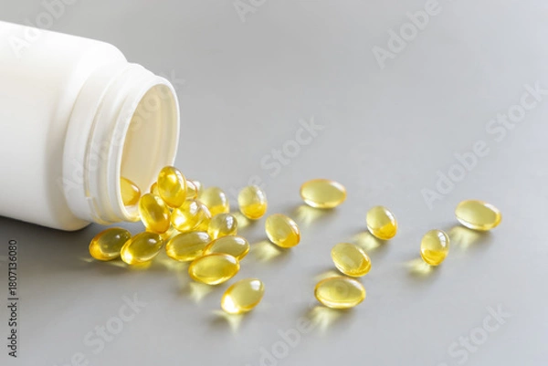 Obraz Yellow softgels (gelatin capsules) and bottle on a grey close up. Omega 3 Fish oil or garlic oil
