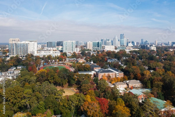 Fototapeta Aerial view of a modern city skyline overlooking a residential neighborhood filled with vibrant autumn trees.