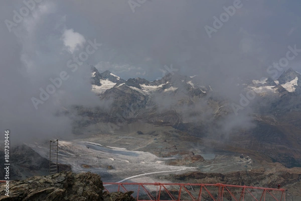 Fototapeta Cloudy day over the Swiss Alps, viewed from Glacier Paradise in Zermatt, with dramatic peaks and misty alpine scenery