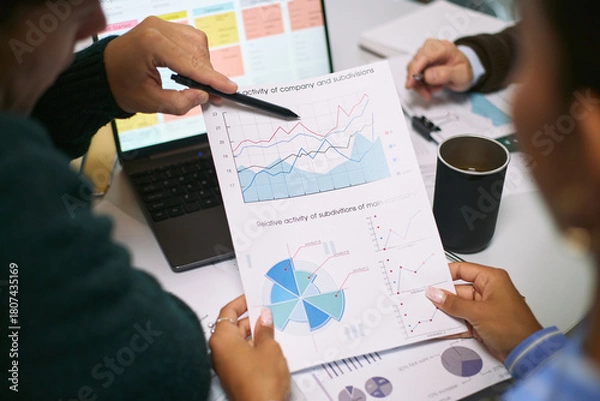 Obraz Caucasian man and Black woman analyzing financial charts and graphs during business meeting, discussing data trends and performance metrics with laptop and documents on desk