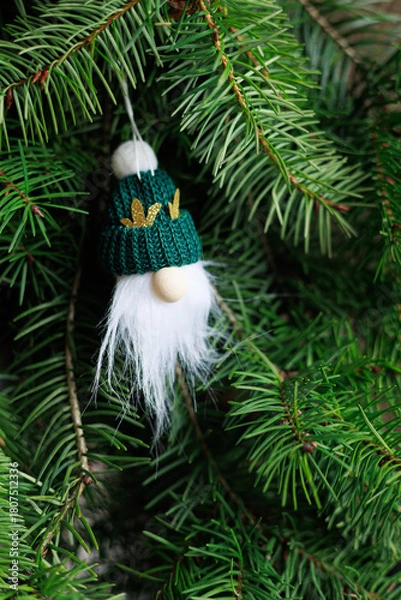 Fototapeta Handmade gnome ornament with green knit hat and white beard on fir branches with authentic natural look, festive mood and soft copy space. Concept of cozy holiday decoration, winter magic.