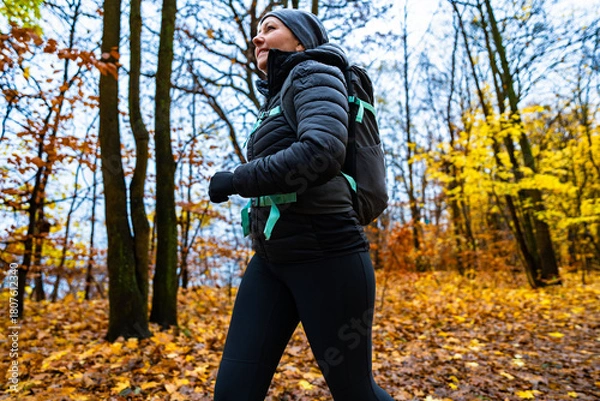 Fototapeta Middle-aged woman training running in forest on autumn day. Side view