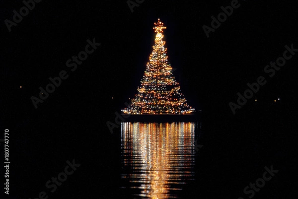 Fototapeta A beautifully illuminated Christmas tree with a star on top, reflecting in the calm water at night.