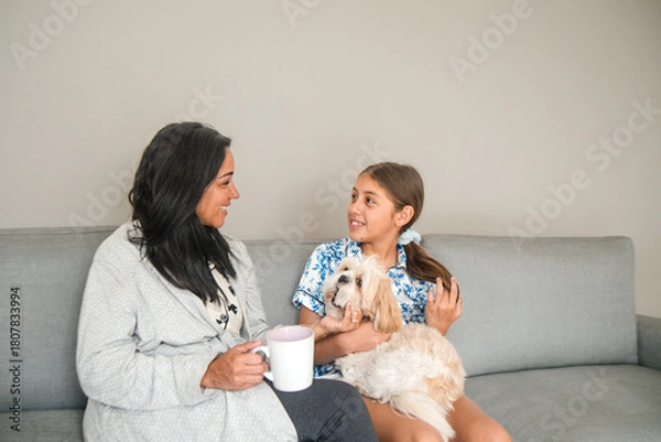Fototapeta A woman and a girl are sitting on a couch with a dog
