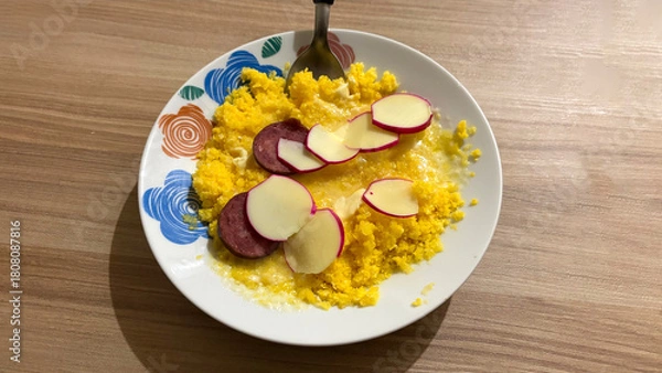 Fototapeta Savory Scramble: A vibrant close-up captures a plate laden with fluffy scrambled eggs, topped with perfectly sliced salami and potatoes, all presented with culinary finesse. 