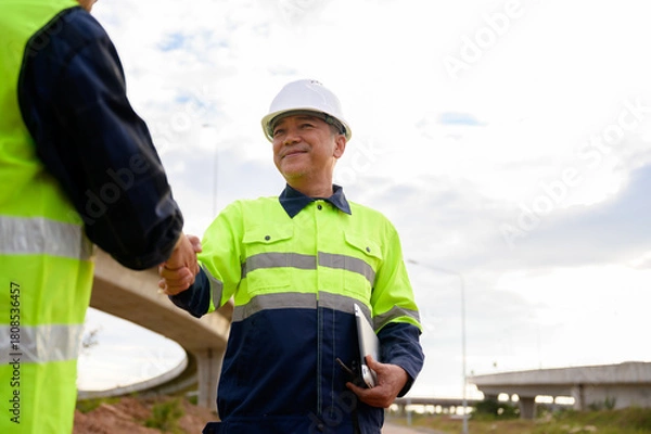 Fototapeta Construction engineers shaking hands at road construction site, showing teamwork, agreement, cooperation, and professional collaboration in civil engineering work.