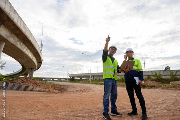 Fototapeta Construction engineers supervise infrastructure work at elevated road construction site. Inspect structure, supervise new road construction, civil engineer working at construction site.