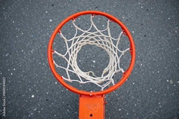 Fototapeta Close up of a weathered basketball on a cracked court with a blurred hoop. A close up, detailed shot of a weathered, scuffed orange basketball resting on cracked asphalt of an outdoor basketball
