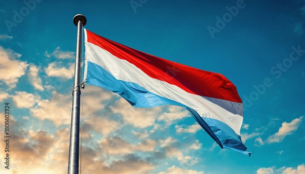 Fototapeta A vibrant Luxembourgish national flag proudly waves against a clear blue sky with soft clouds, symbolizing national identity and freedom for the nation
