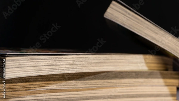 Fototapeta Macro-like view of books arranged with one leaning open, showcasing layered pages and contrast lighting, great for storytelling themes and printed media backgrounds.