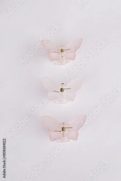Fototapeta Three butterfly-shaped hair clips are placed on a clean white background, creating a simple and elegant look