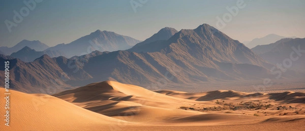 Obraz AI-generated image - A wide desert landscape with soft golden sand dunes and rugged mountains in the distance, captured in warm natural light for a serene and dramatic atmosphere.