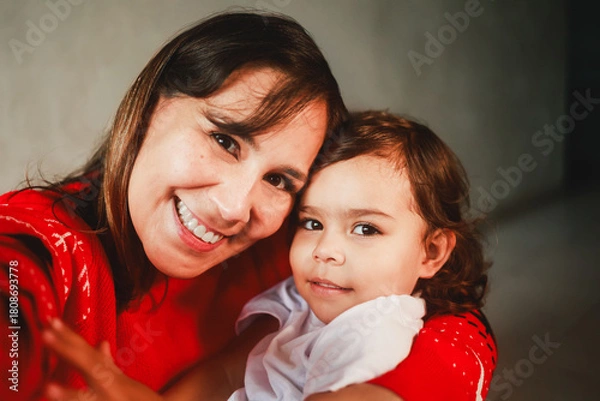 Fototapeta Latin mother and child having fun during Christmas time. Mom and toddler daughter taking self picture together