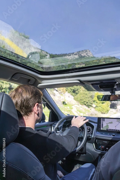 Obraz A focused driver sits behind the wheel in a modern car, navigating busy city streets. A large GPS display guides the route, highlighting the tech-enabled, urban driving experience.