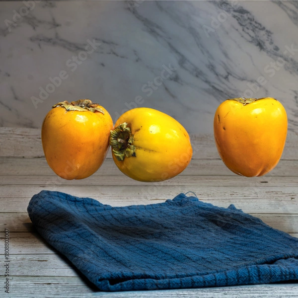 Obraz  three fresh persimmons floating above blue cloth on wooden surface