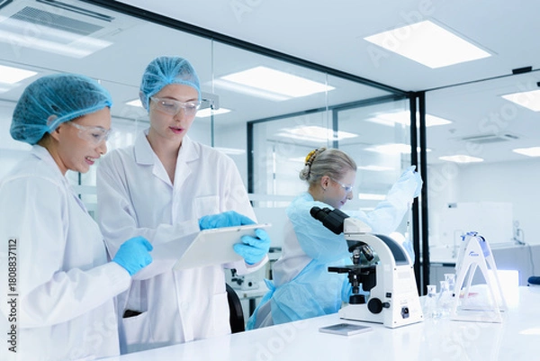 Fototapeta A senior scientist mentors a junior colleague in a modern lab, using a tablet to guide her through a precise pipetting technique, fostering hands-on learning and skill development.