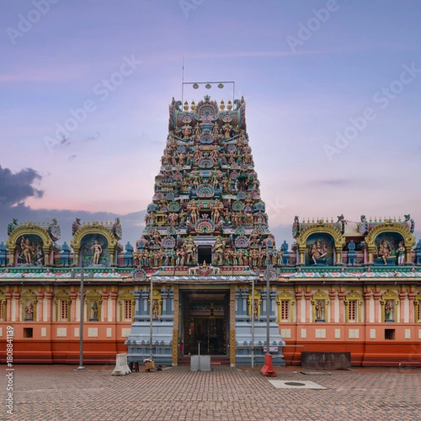 Fototapeta Vibrant Kandaswamy Kovil Hindu temple in Kuala Lumpur, Malaysia, featuring an intricately carved gopuram with colorful deities against a soft twilight sky.