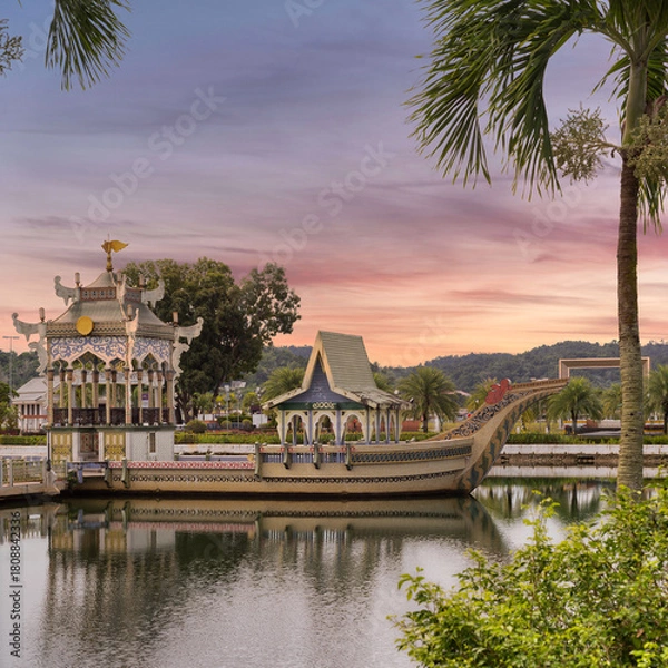 Fototapeta Mahligai Royal Barge on a lake at Sultan Omar Ali Saifuddien Mosque, Bandar Seri Begawan, Brunei. Ornate boat under a vibrant sunset sky, framed by palm fronds.