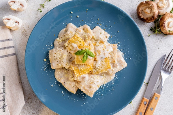 Fototapeta a plate of ravioli, filled with a butternut squash mixture, served in a creamy white sauce. It is garnished with grated Parmesan cheese, dried herbs, and a fresh basil leaf, with fresh mushroom