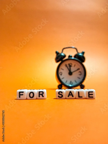 Fototapeta The letter cubes spelling "FOR SALE" are located in front of the small clock, symbolizing real estate listings, time and real estate opportunities.