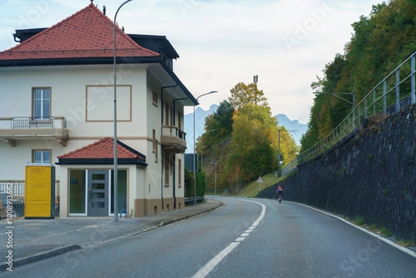 Obraz man rides bicycle on quiet and empty mountain road in small alpine town