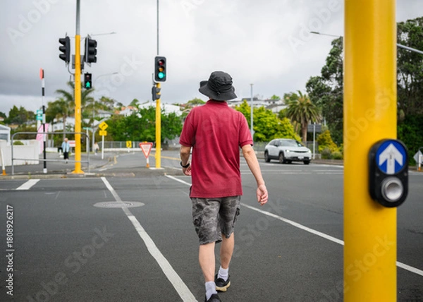 Obraz Man walking across the street with green pedestrian crossing light on. Auckland.