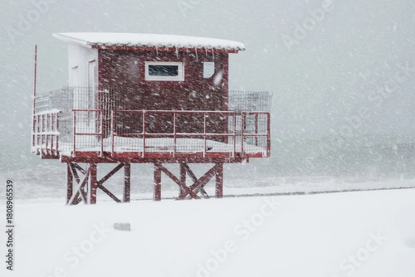 Fototapeta Red lifeguard tower construction on the coast during heavy snowing