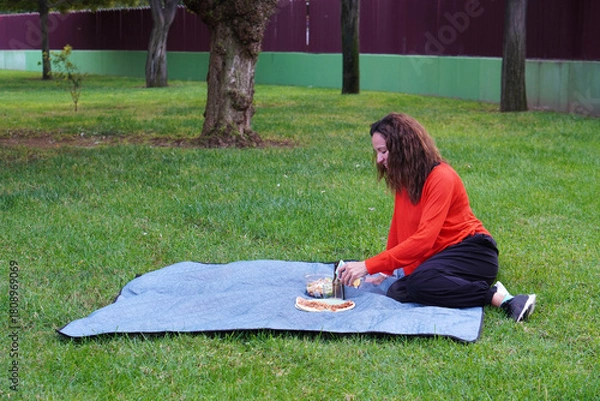 Fototapeta woman preparing a picnic lunch in a park pizza and salad