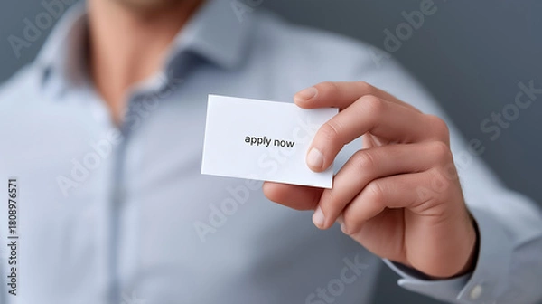 Fototapeta Man in a formal shirt holding a white business card with the words apply now on it, symbolizing a direct invitation for job seekers and career opportunities with copy space