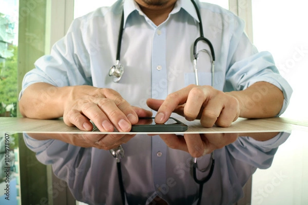 Obraz Doctor using smartphone at desk with stethoscope