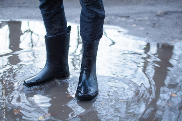 Fototapeta Legs of a man in rubber boots walking on deep puddle