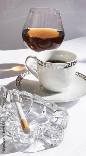 Fototapeta Copa, café y cigarrillo.
Coñac junto al café con un cenicero y un cigarrillo.
