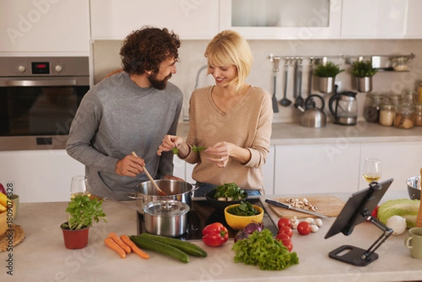 Fototapeta Two people are happily cooking in a bright kitchen, chopping fresh vegetables and sharing moments of joy while preparing a delicious meal together.