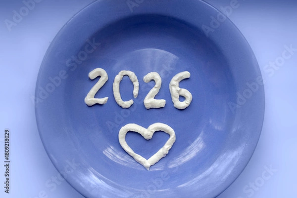 Fototapeta Dairy products in new year. Numbers 2026 and heart made of cream on blue plate.