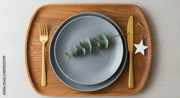 Obraz Wooden charger with gray plate and brass cutlery. Eucalyptus sprig and small white ornament completing placement.  Nordic style Christmas table setting, wood, gray, gold accents