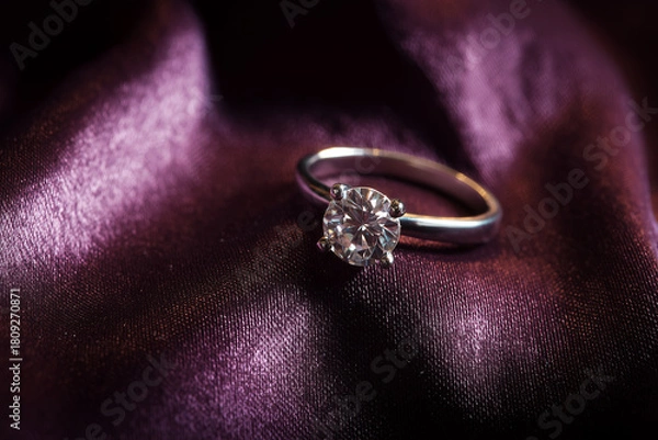 Obraz Pierścionek zaręczynowy położony na eleganckim materiale w miękkim świetle