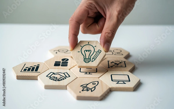 Fototapeta Hand placing a lightbulb icon on a wooden hexagon puzzle symbolizing creative ideas and innovative solutions for business growth and strategic planning on a white surface