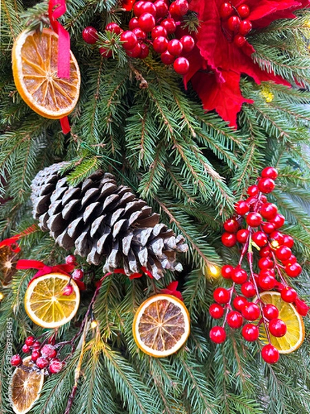 Obraz Festive holiday decoration featuring pine cone, dried orange slices, red berries, and evergreen branches, creating a warm and inviting atmosphere with vibrant colors and textures. Vertical background