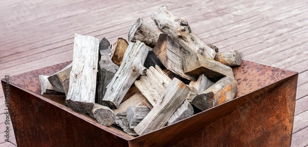 Fototapeta A pile of firewood stacked in a metal container. The wood pieces vary in size and texture, suitable for outdoor fires or heating