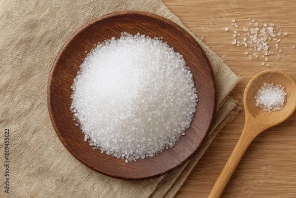 Fototapeta Wooden plate piled high with white salt crystals, beside a wooden spoon with more salt