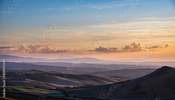 Fototapeta Hills And Valleys Under A Golden Sunrise Sky With Wispy Clouds In A Rural Landscape