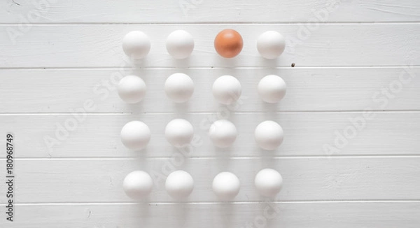 Fototapeta White raw eggs with one brown egg in rows on a white wooden table